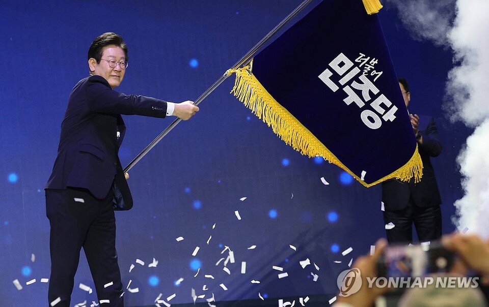 더불어민주당 당대표 연임에 성공한 이재명 신임 당대표가 18일 오후 서울 송파구 올림픽공원 KSPO돔에서 열린 전국당원대회에서 박찬대 대표 직무대행 겸 원내대표로부터 전달받은 당기를 흔들고 있다(연합뉴스)