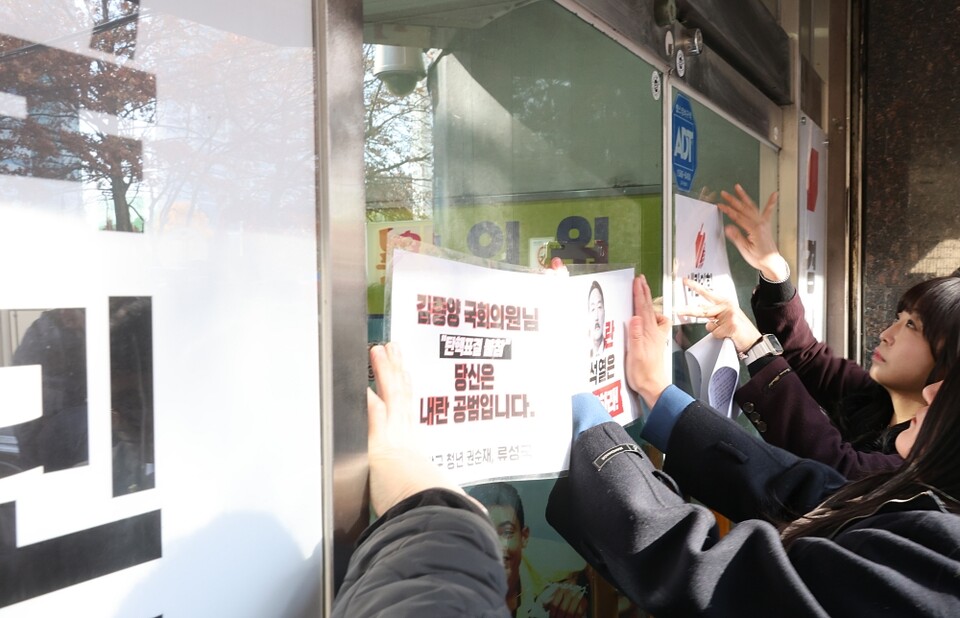 더불어민주당 경남도당 청년위원회 관계자들이 11일 오후 경남 창원시 국민의힘 경남도당 당사 건물 출입문 앞에 국민의힘 의원들의 대통령 탄핵 표결 불참에 항의하는 문구가 적힌 피켓을 부착하고 있다 (사진=연합뉴스)