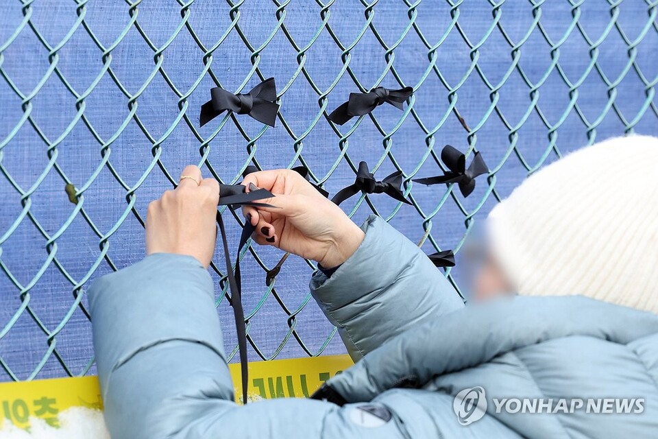 지난달 11일 오전 무안국제공항에서 제주항공 여객기 참사 유가족들이 사고 현장 인근 철조망에 검은 리본을 달고 있다. (무안=연합뉴스)