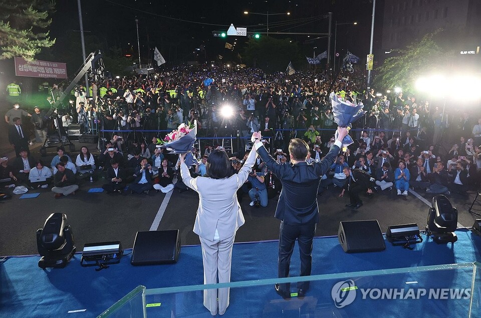 제21대 대통령 당선이 확실시되는 더불어민주당 이재명 대선 후보와 부인 김혜경 여사가 4일 서울 여의도 국회 인근에서 당 주최로 열린 국민개표방송 행사에 참석해 꽃다발을 받고서 시민들을 향해 두 팔을 들어 인사하고 있다. (서울=연합뉴스)